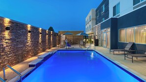A swimming pool with a stone wall on one side and a modern building on the other.