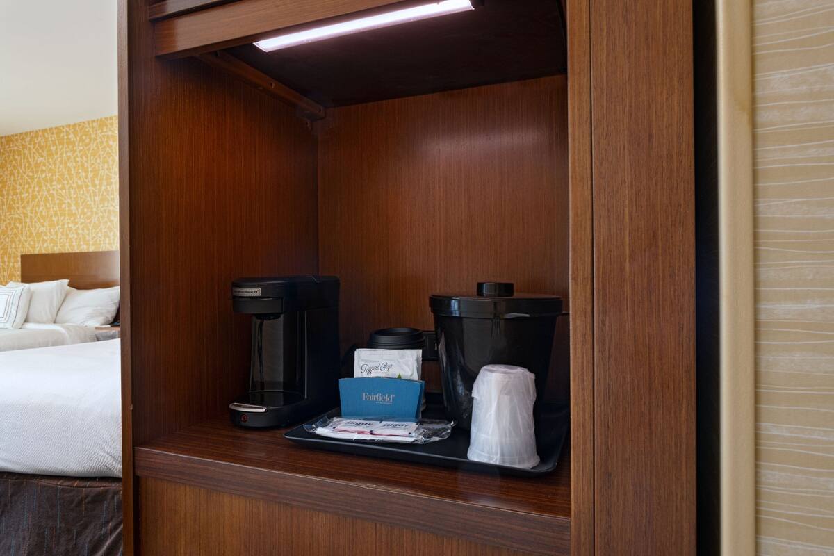 Una camera d'albergo con un armadietto in legno che contiene una macchina per il caffè, una scatola di fazzoletti e un cestino.