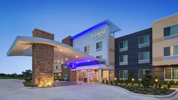 A Fairfield Inn & Suites hotel with a modern design, featuring a stone facade, a covered entrance, and a well-lit exterior.