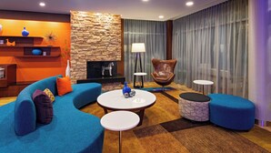 A modern living room with a curved blue sofa, a fireplace, a stone accent wall, and a large window with sheer curtains.