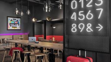 A modern workspace with a large table, multiple stools, a laptop, and a red suitcase.
