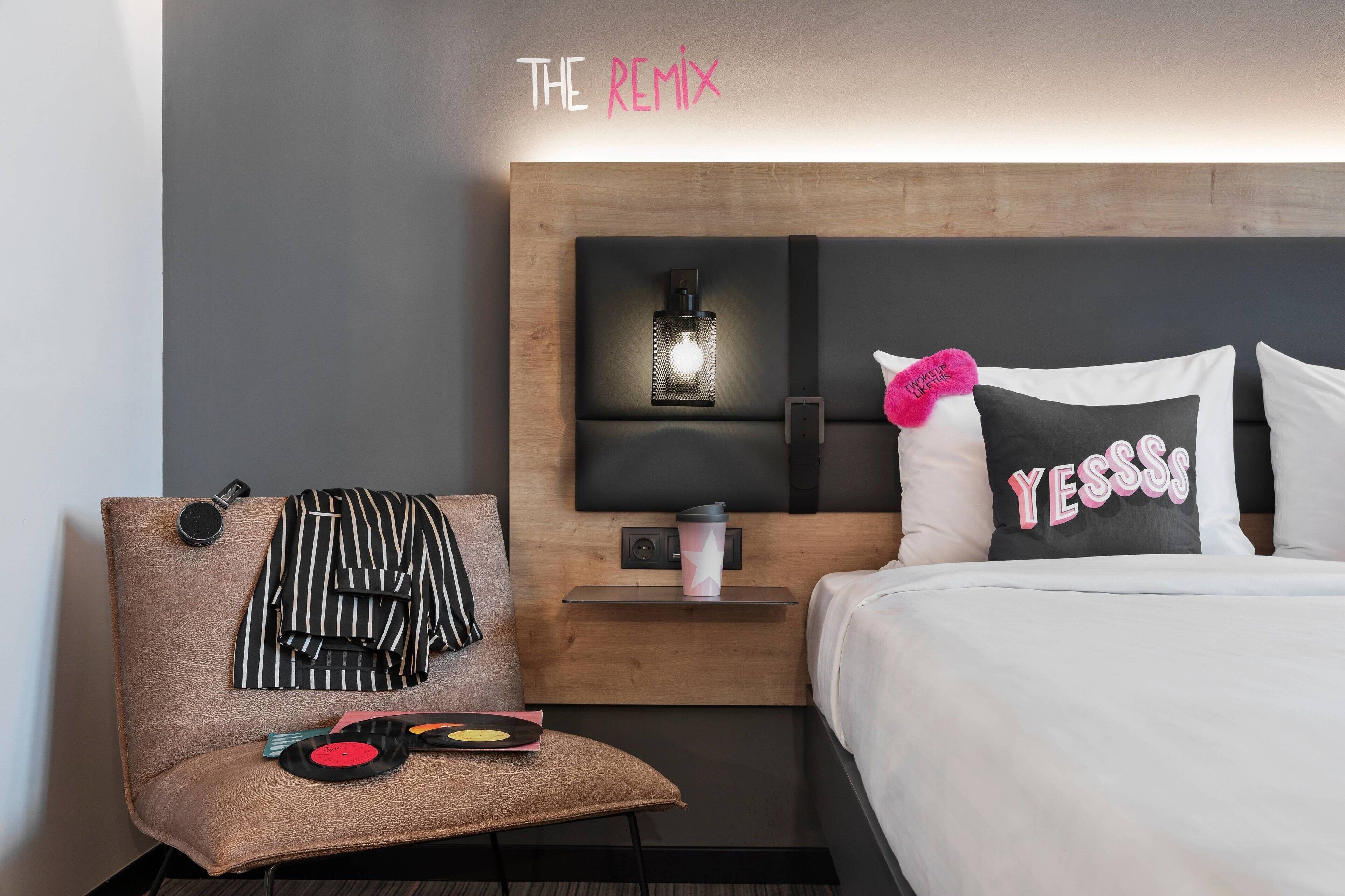 Una habitación de hotel con una cama, una mesita de noche, una silla y un estante en la pared.