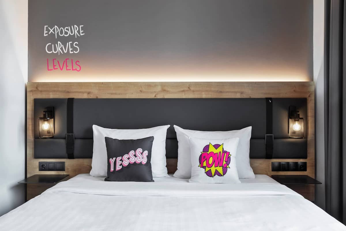 A modern hotel room with a wooden headboard, two bedside lamps, and two decorative pillows with bold text.