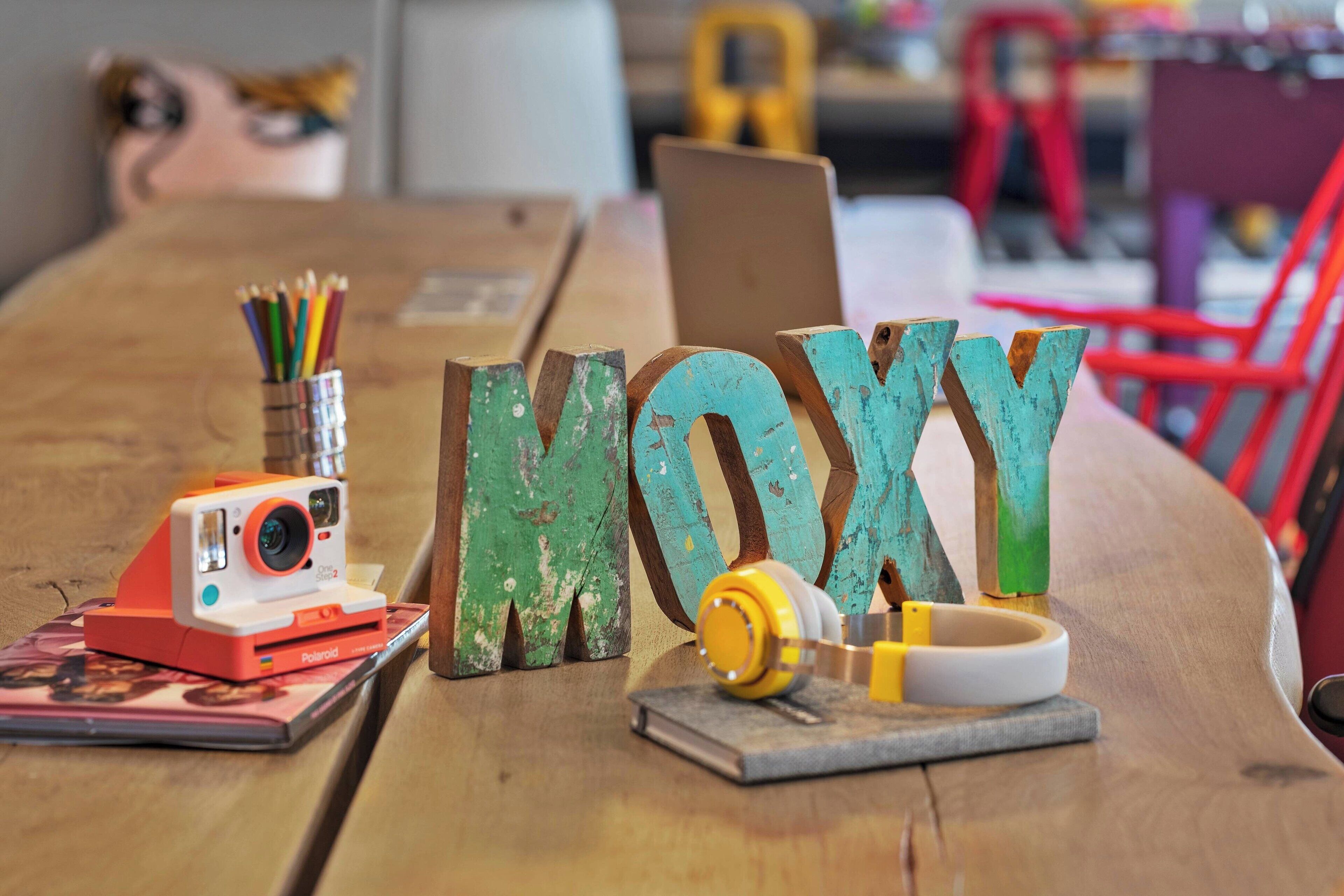 A wooden table with a Polaroid camera, colorful pencils, and a pair of headphones.