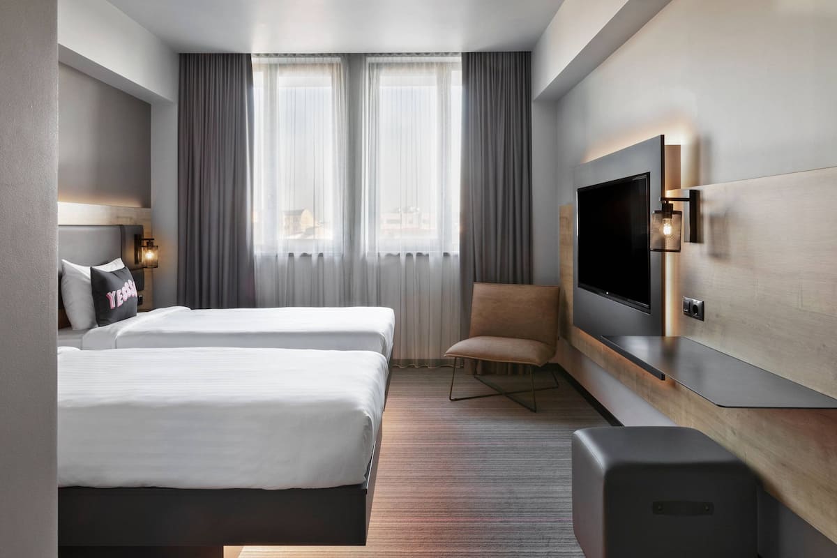 A hotel room with two beds, a TV, a chair, and a large window with curtains.