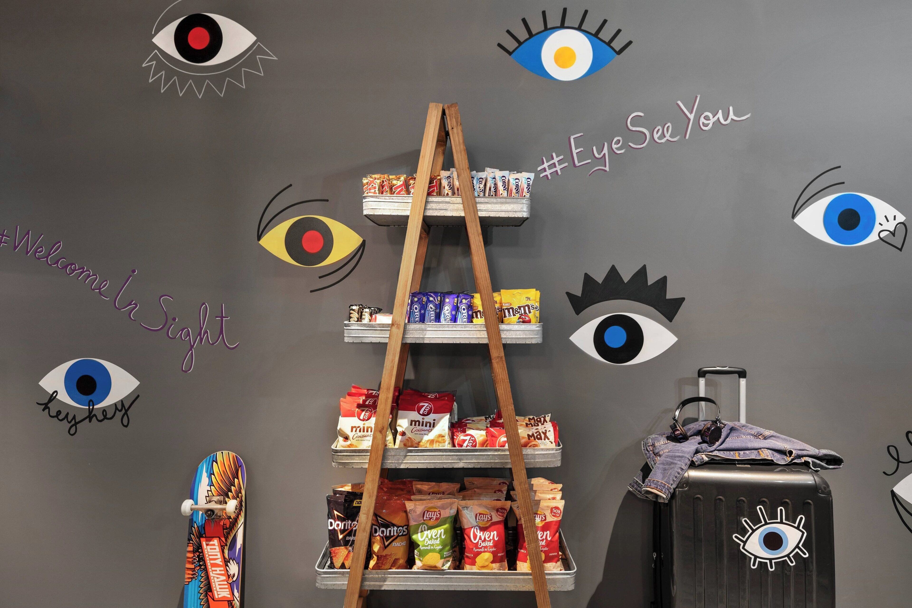 Una pared con estantes que muestran aperitivos, una escalera y una maleta con un diseño de ojo.