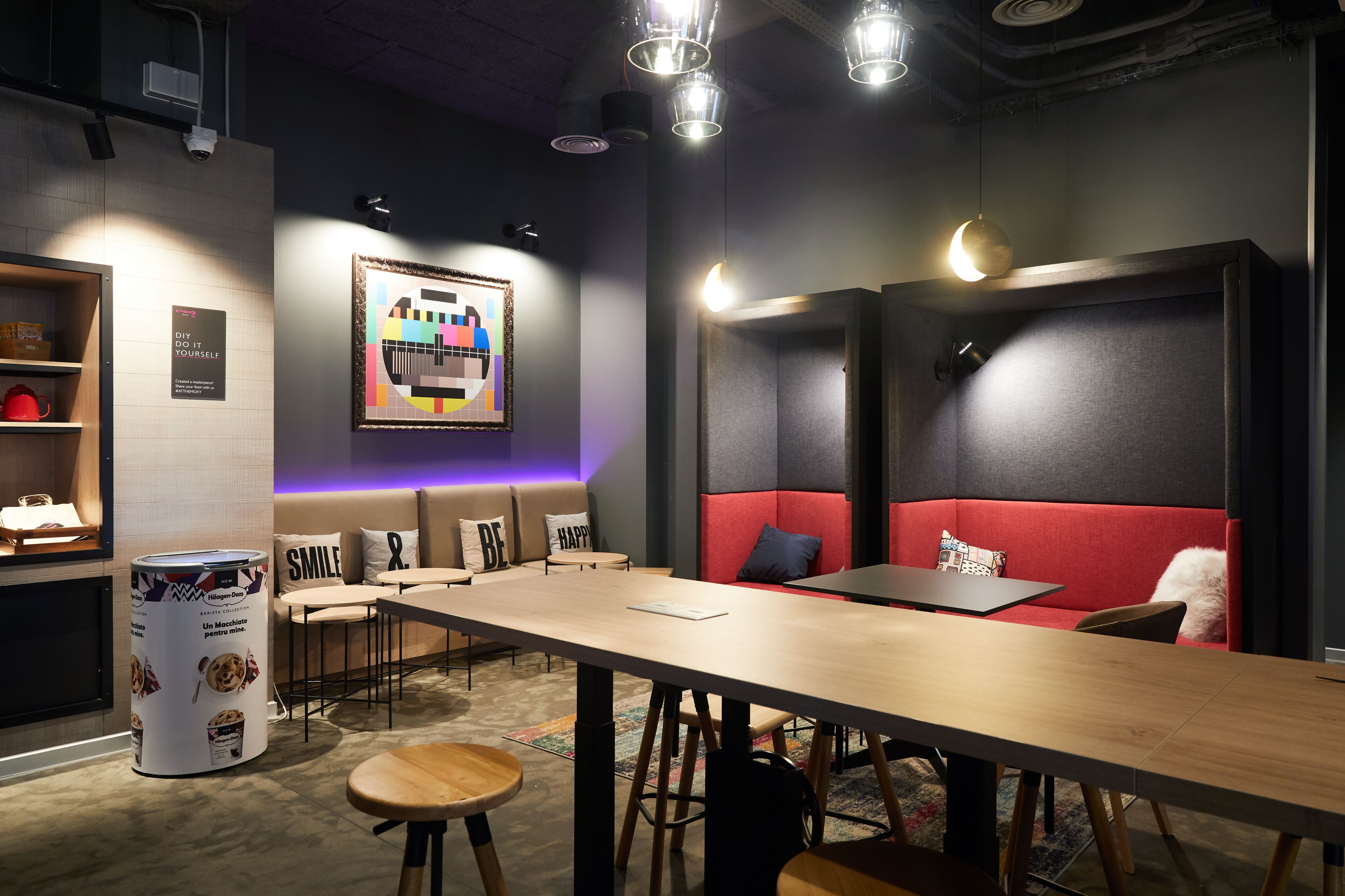 A modern interior with a long table, red seating, and a wall-mounted digital art piece.
