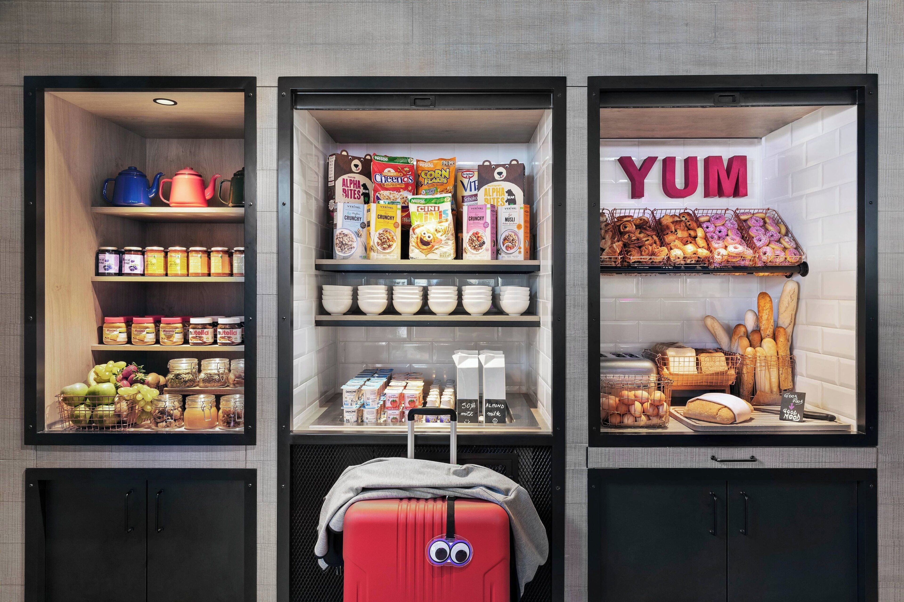 A kitchenette with a variety of food items, including cereals, condiments, and a display of baked goods.