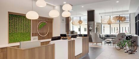Un área de recepción moderna con un mostrador de madera, pared verde e iluminación contemporánea.