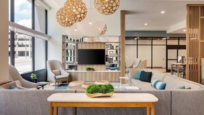 A modern living room with a large sofa, a coffee table, and a TV mounted on the wall. There are two large pendant lights hanging from the ceiling. - Element by Marriott Iowa City (Iowa City)