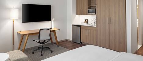 Habitación de hotel con cama, escritorio, silla, televisor, microondas y lavavajillas.