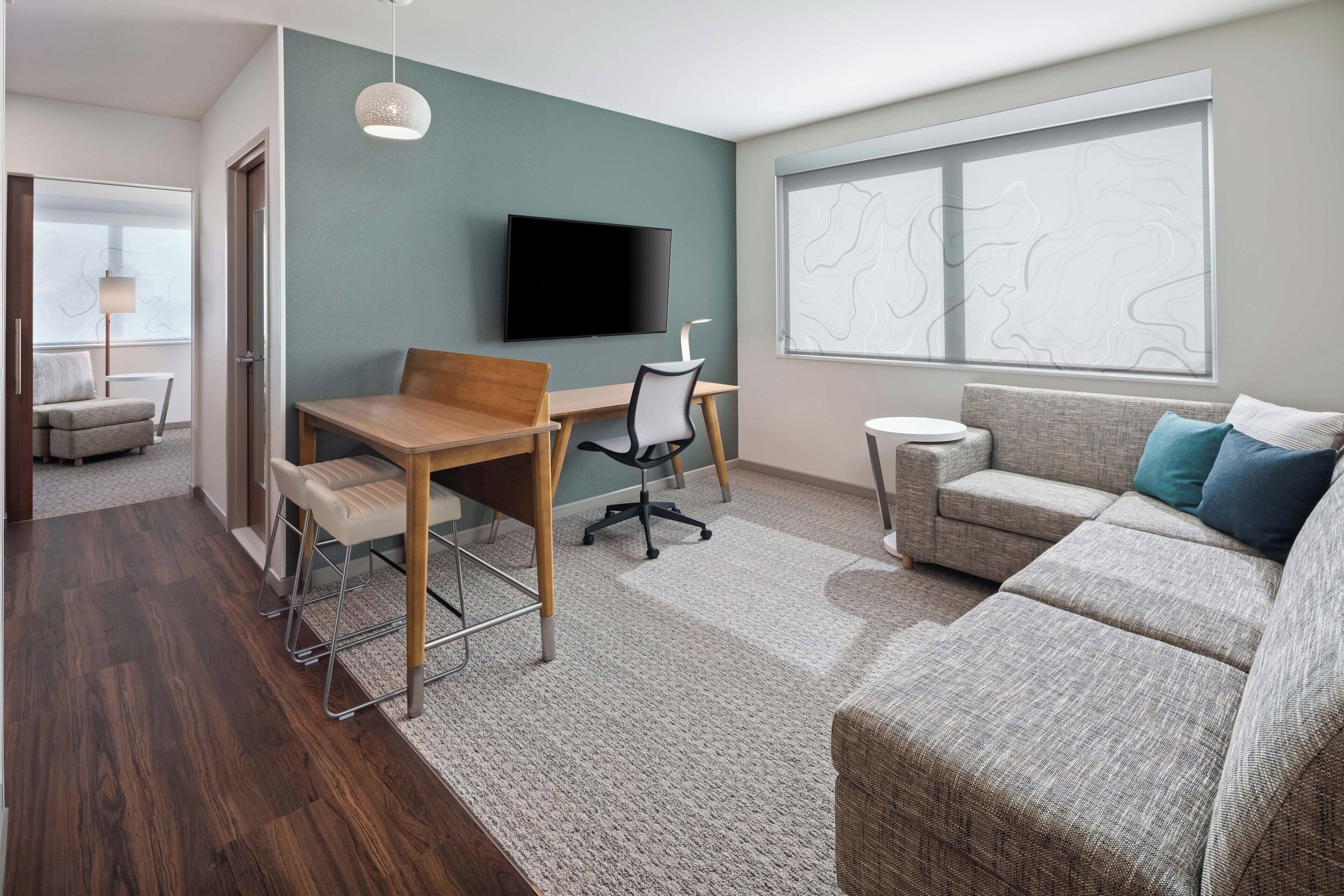 Una sala de estar moderna con una mesa de comedor de madera, un sofá gris y un televisor de pantalla plana montado en la pared.