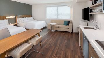 Ett hotellrum med två sängar, en soffa, ett matbord, en TV och ett litet kök.