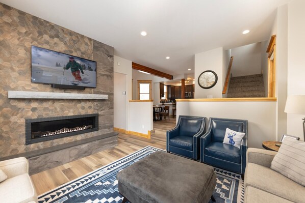 A living room with a stone wall, a fireplace, a television, and a dining area in the background. - French Street Estate: House and Carriage House, Private Hot Tub, Downtown (Breckenridge)