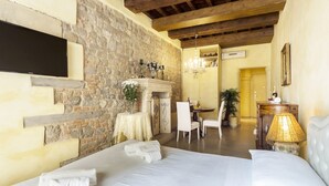 A hotel room with a stone wall, wooden beams, a bed with white linens, a small table with a vase, and a chandelier. - Love Honeymoon Apartment Piazza Signoria View WiFi AC (Firenze)