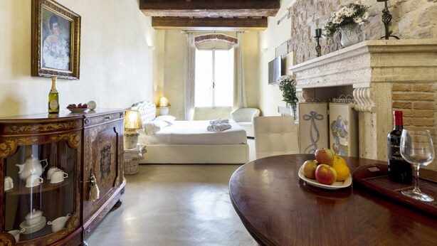 A room with a bed, a dining table with fruit and wine, a fireplace, and a stone wall. - Love Honeymoon Apartment Piazza Signoria View WiFi AC (Firenze)