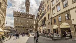 A historic square with a prominent clock tower, surrounded by traditional buildings with cafes and shops. - Love Honeymoon Apartment Piazza Signoria View WiFi AC (Firenze)