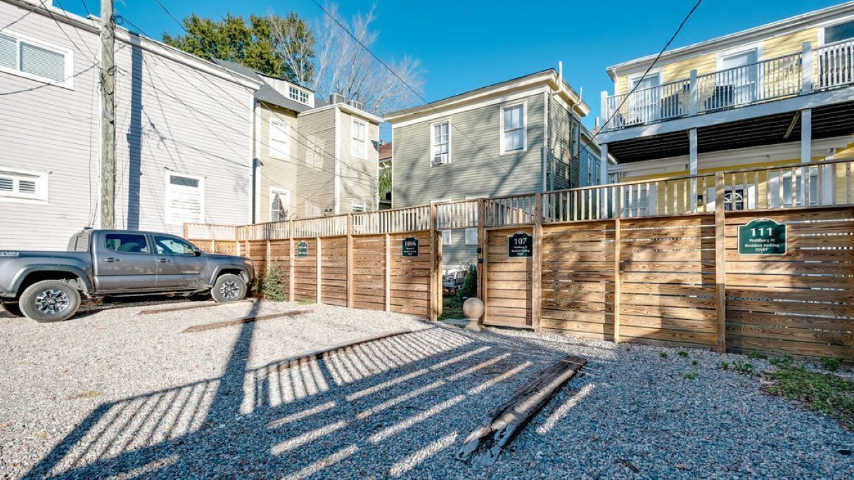 A gated residential area with numbered wooden fences, a gravel driveway, and a parked truck.