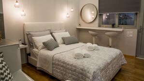 A modern bedroom with a large bed, bedside tables, a round mirror, a window with a view, and a built-in sink. - Luxury guesthouse nature (Nafplio)
