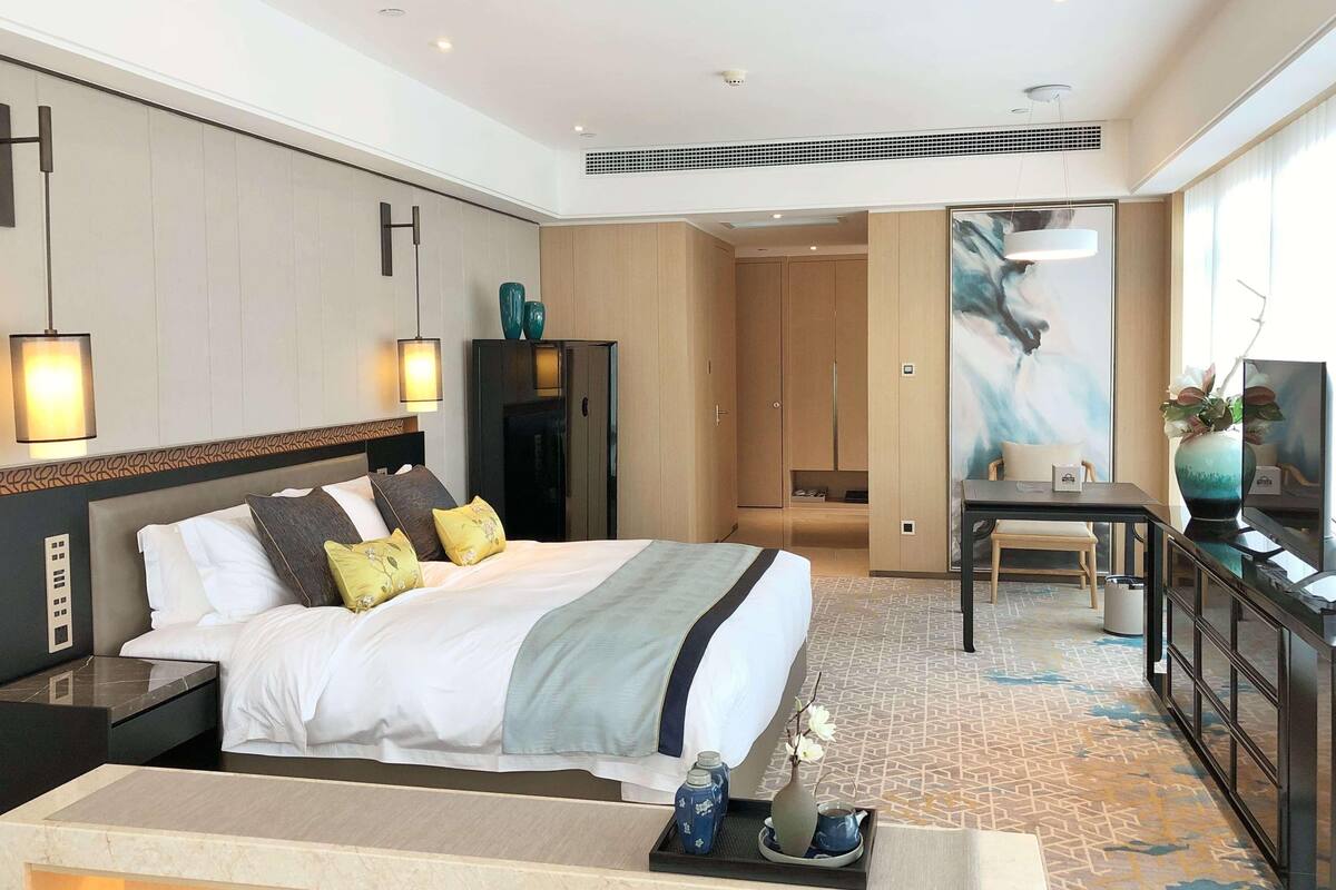 Une chambre d’hôtel comprenant un lit, des tables de chevet, un bureau, une chaise, une armoire, un tableau et un vase.