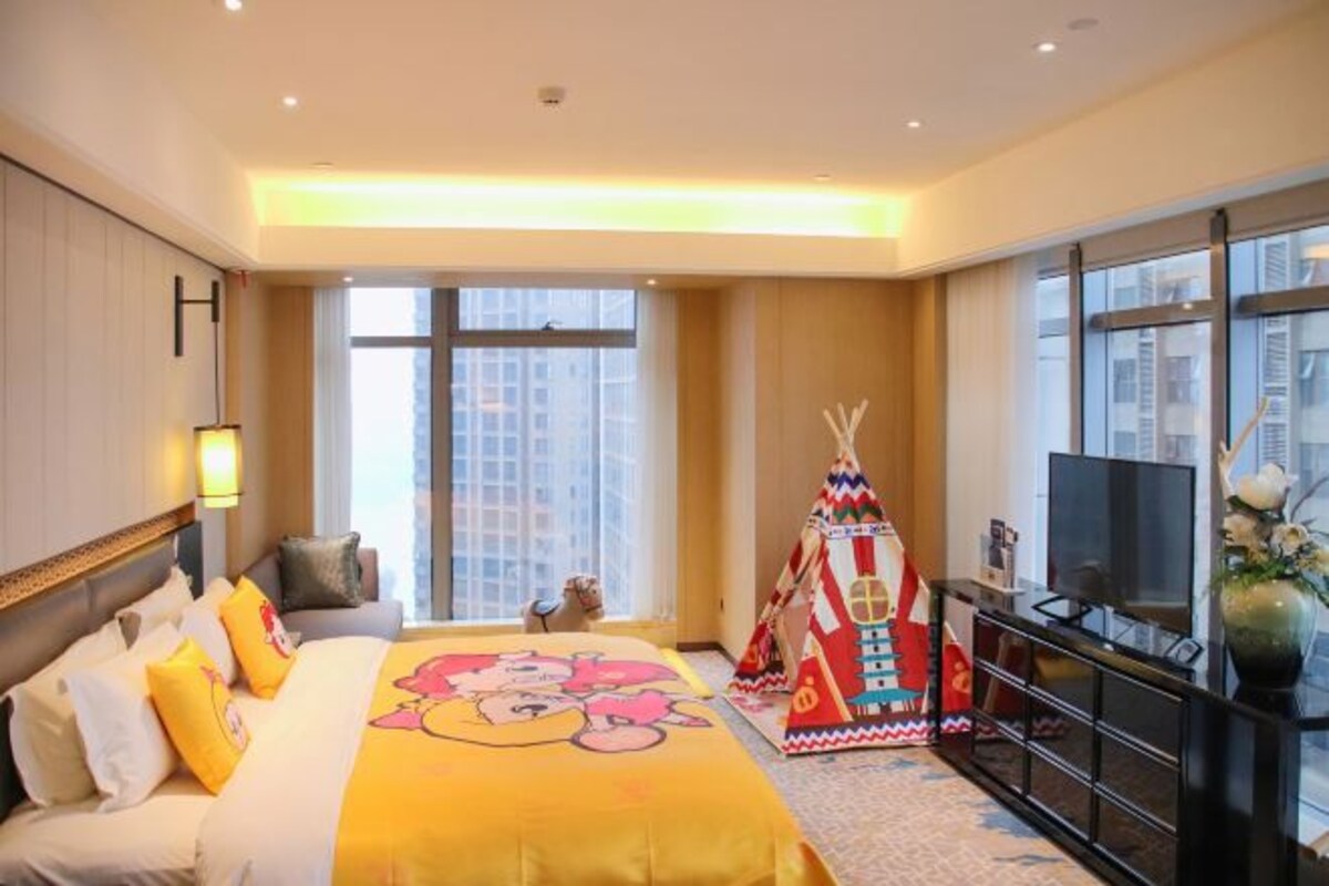 Quarto de hotel com uma cama grande, televisão, penteadeira e janela com vista para a cidade.
