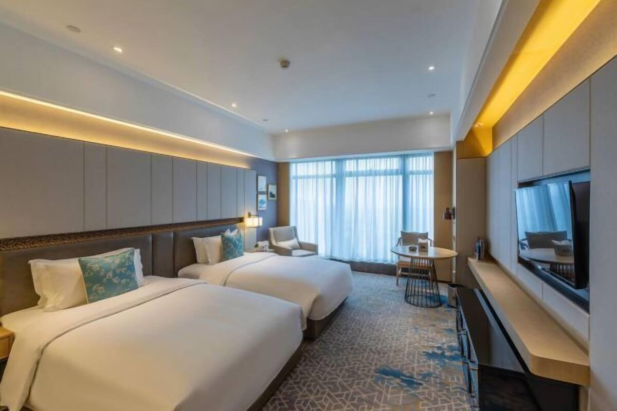 Une chambre d’hôtel avec deux lits, une télévision, un bureau et une grande fenêtre avec des rideaux.