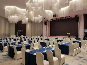 Une salle de conférence avec des rangées de tables, des chaises et une scène.