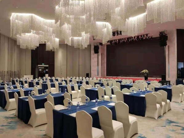 Sala de conferências com mesas, cadeiras e um palco em disposição alinhada.