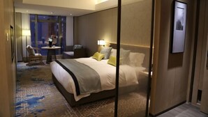 A hotel room with a large bed, a desk, a chair, and a view of the city through large windows. - Days Hotel Suites By Wyndham Zixin Changsha (Changsha)