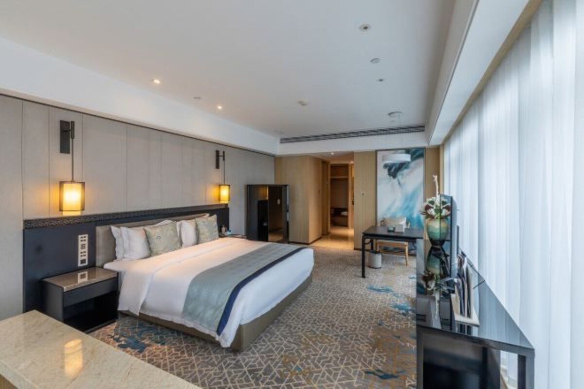 Une chambre d’hôtel moderne avec un grand lit, des tables de chevet, un bureau et une grande fenêtre.