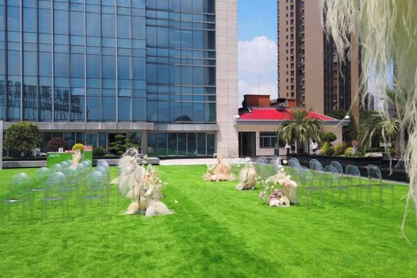 A grassy outdoor area with clear glass windows of a building in the background.