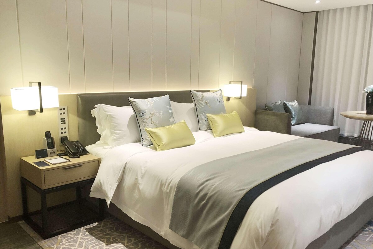 Une chambre d’hôtel avec un grand lit, des lampes de chevet, une table de chevet avec un téléphone et une lampe, et une petite table avec un vase.