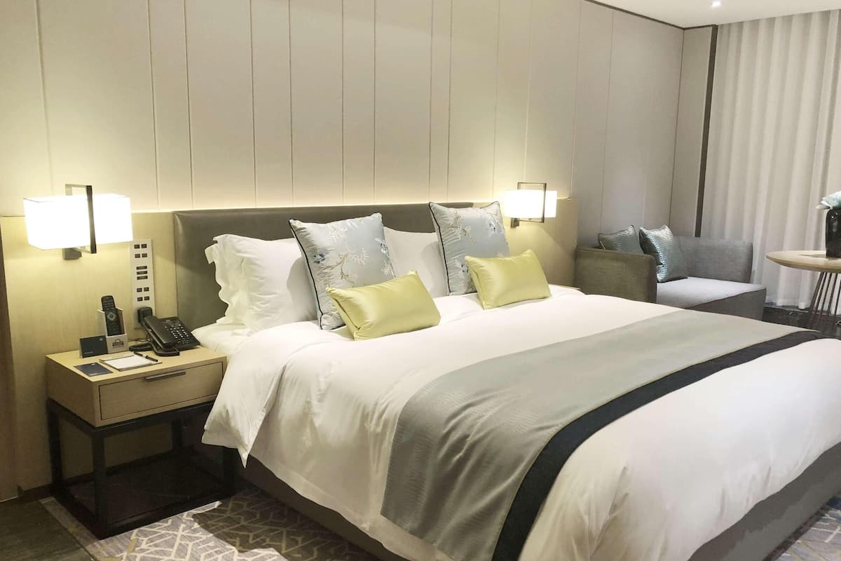 Une chambre d’hôtel avec un grand lit, des lampes de chevet, une table de chevet avec un téléphone et une lampe, et une petite table avec un vase.