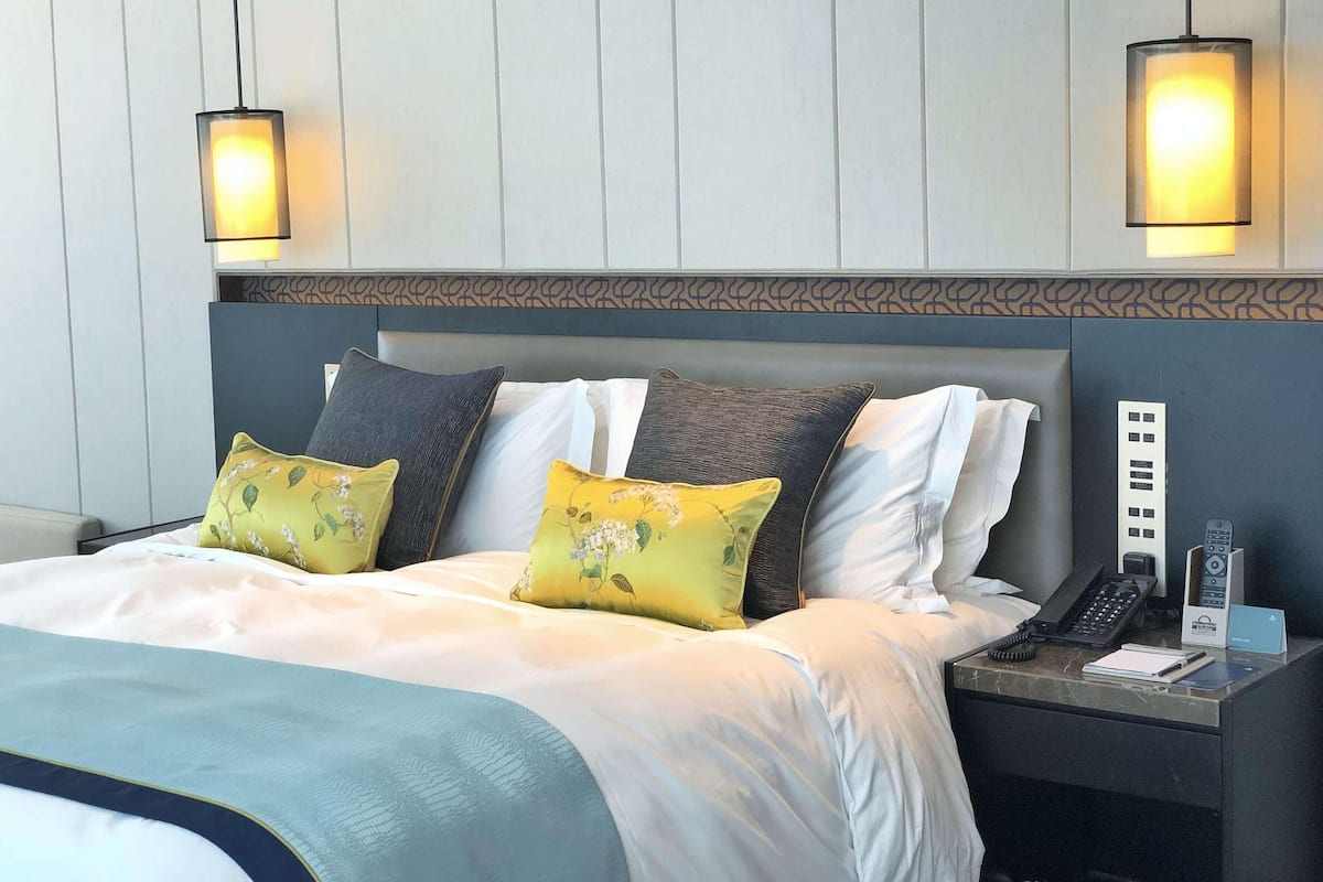 Une chambre d’hôtel comprenant un lit, deux lampes de chevet, une table de chevet avec un téléphone et un panneau de commande fixé au mur.
