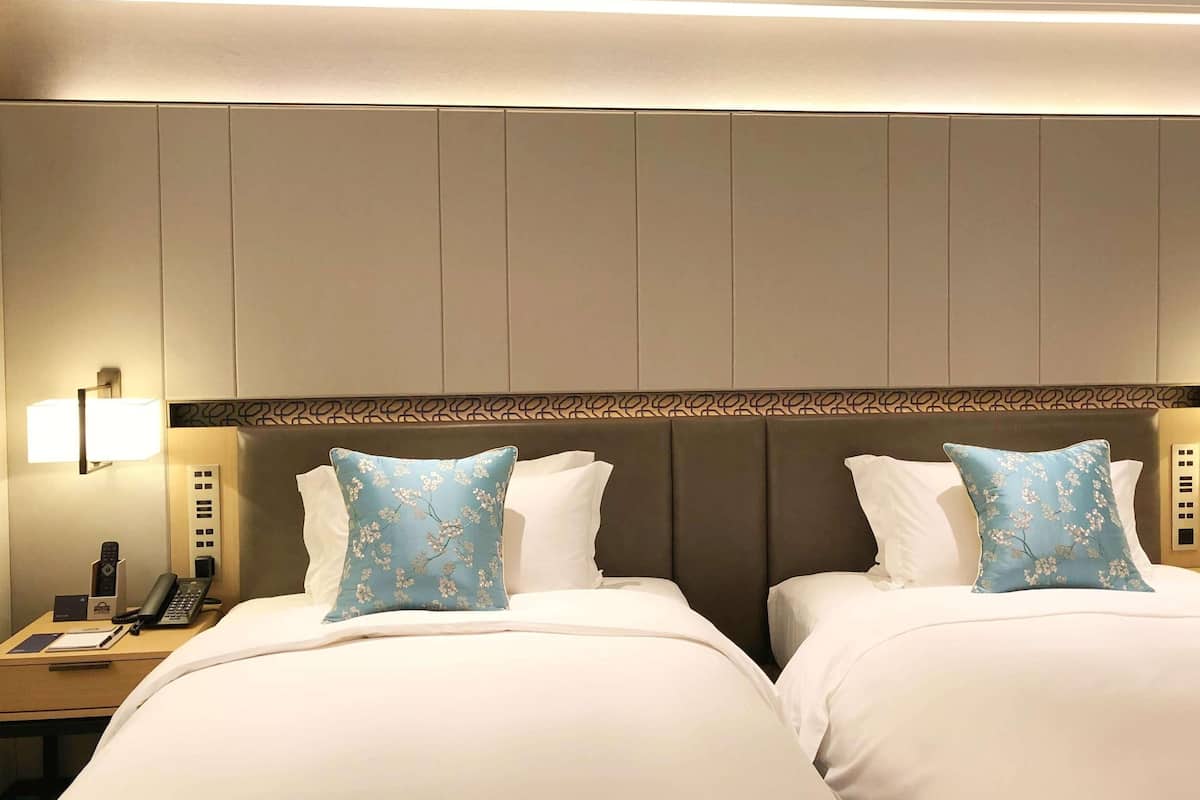 Une chambre d’hôtel avec deux lits, une table de chevet avec un téléphone et une lampe, et une tête de lit à motifs.