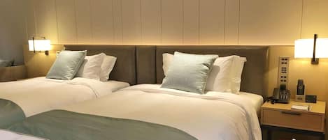 A hotel room with two beds, bedside lamps, a nightstand with a phone and a box of tissues.
