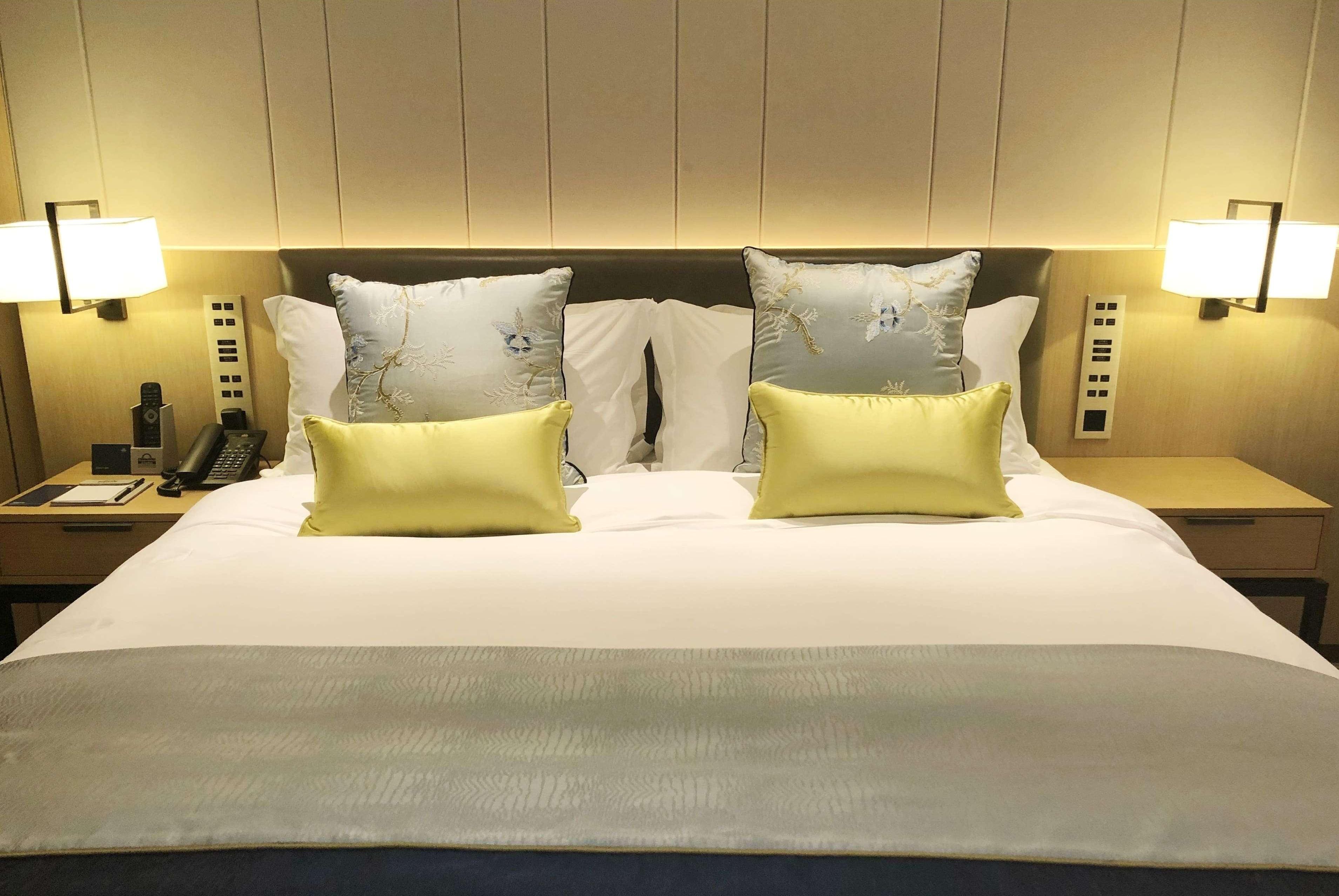 Quarto de hotel com uma cama grande, duas mesas de cabeceira, telefone e luminárias fixadas na parede.