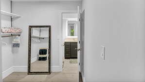 A hallway with a mirror, a closet with hanging clothes, and a kitchen area visible through an open door. - One Bedroom Steps Away From The Beach | Pool! (Sunny Isles Beach)