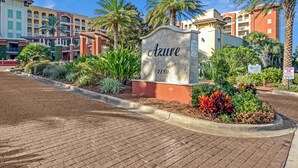 A hotel entrance with a sign reading "Azure 1150" surrounded by landscaped gardens and palm trees. - Azure 118 ~ 4BR Beachfront Ground Floor Corner Condo ~ Sleeps 14 ~ Must See! (Fort Walton Beach)