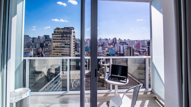 Balcón con una laptop, una silla y una mesa, con vista a un paisaje urbano lleno de edificios.