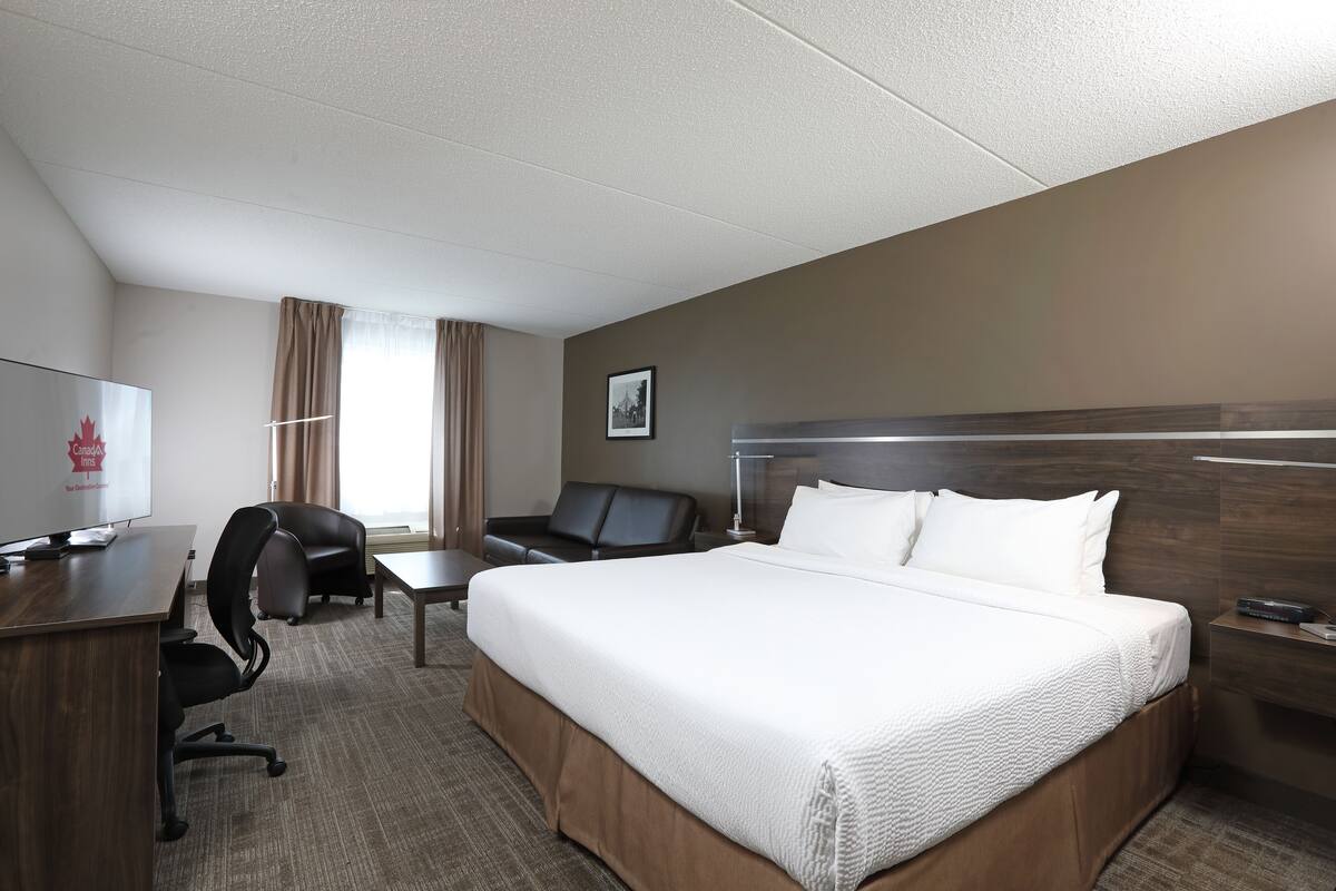 A hotel room with a large bed, a desk with a chair, a television, and a window with curtains.