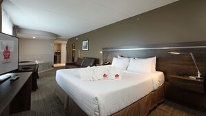 Ein Hotelzimmer mit Bett, Schreibtisch, Stuhl, Nachttisch, Lampe und Fernseher.