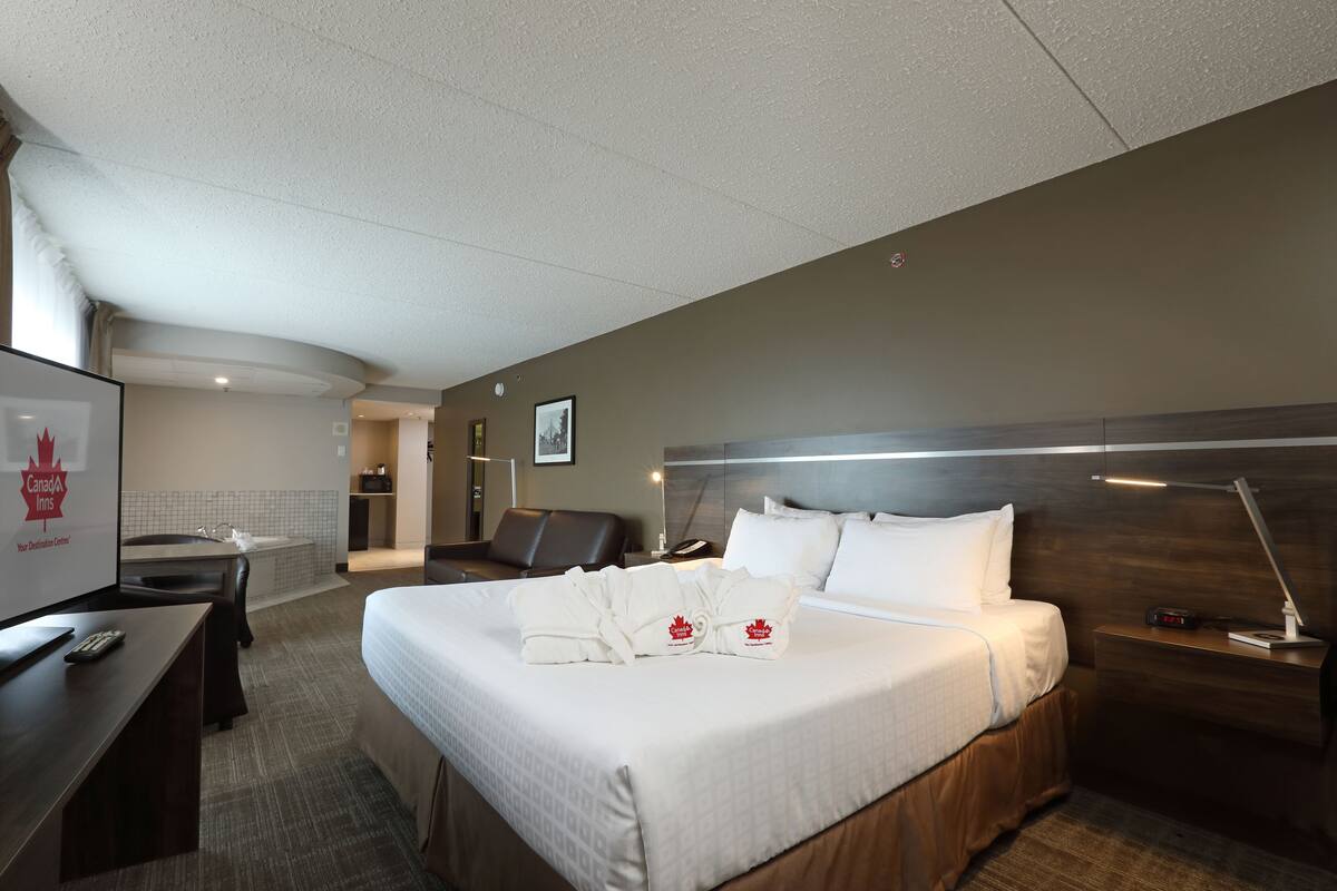 A hotel room with a bed, a desk, a chair, a nightstand, a lamp, and a TV.