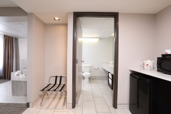 Un baño moderno con inodoro, lavamanos y un refrigerador pequeño negro.