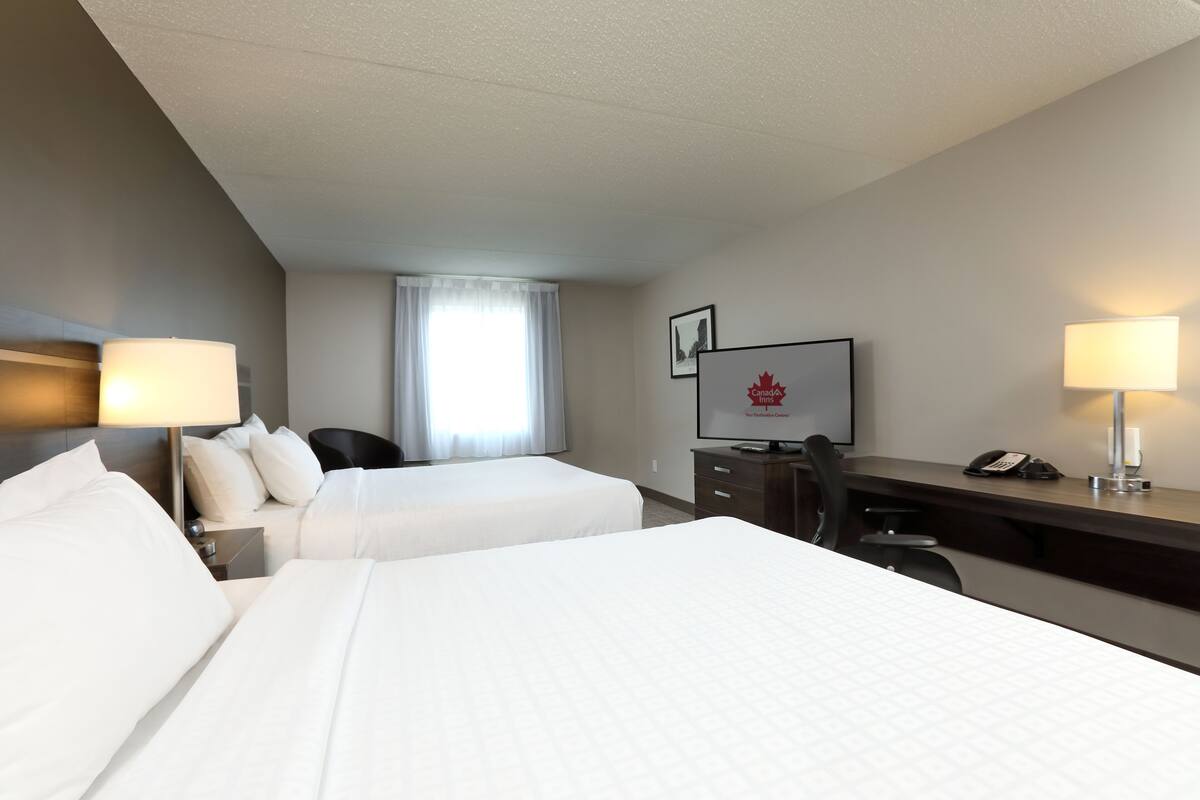 A hotel room with two beds, a desk, a chair, a television, and a telephone.