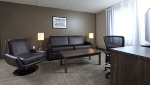 Ein Hotelzimmer mit einer schwarzen Ledersofa, einem schwarzen Ledersessel, einem Holztisch, einem Schreibtisch und einer Lampe.