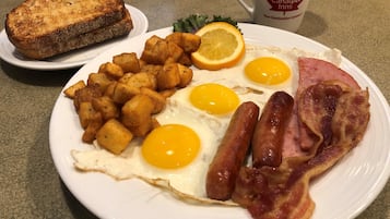 Une assiette de petit-déjeuner comprenant des œufs, du bacon, des pommes de terre rissolées, des toasts et une tranche d’orange.