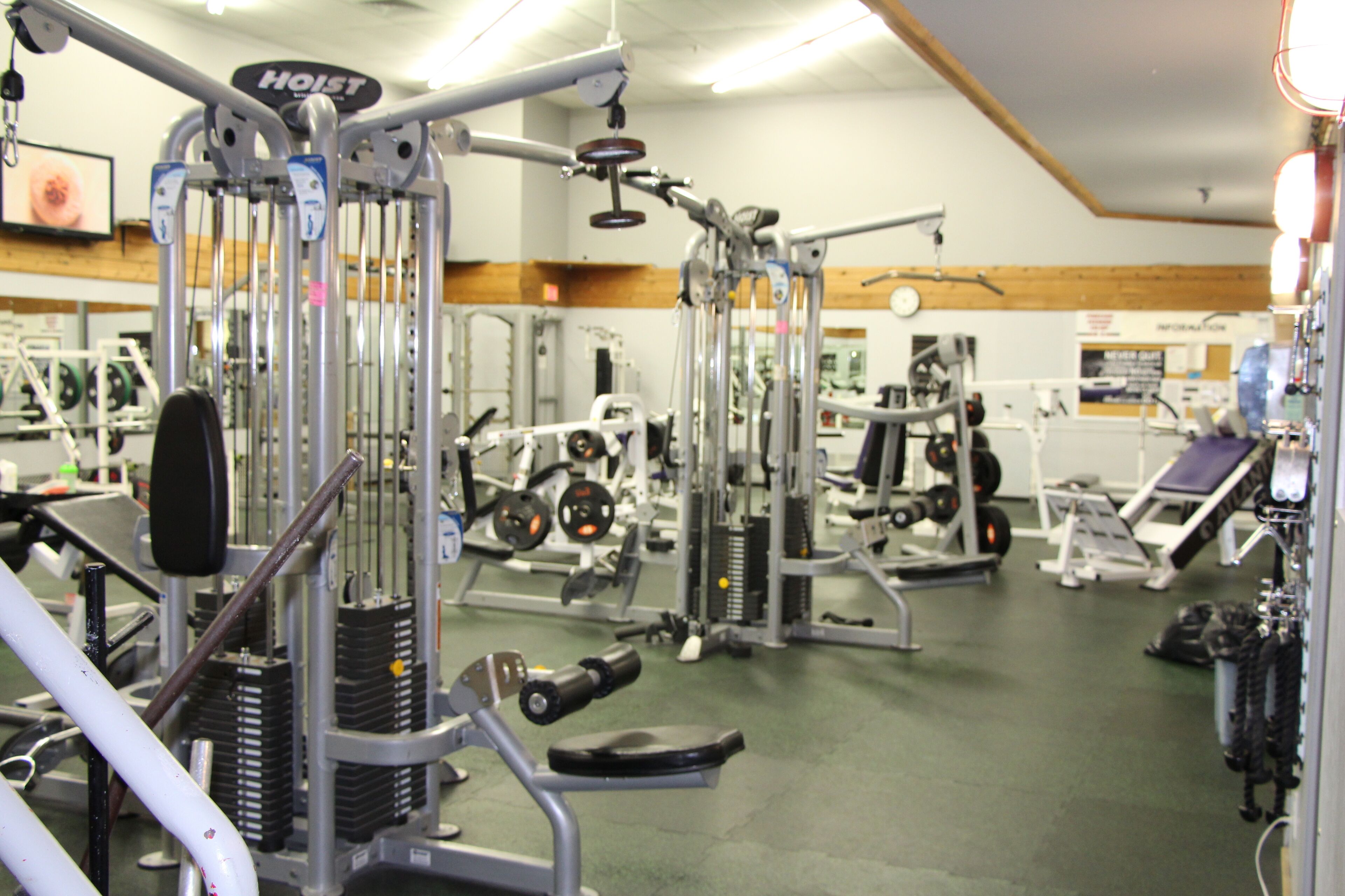 Un gimnasio con diferentes máquinas de ejercicio, pesas apiladas y un espejo grande.