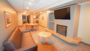 A living room with a brown leather sofa, a wooden coffee table, a fireplace, and a television mounted on the wall. - Canad Inns Destination Centre Portage la Prairie (Portage La Prairie)
