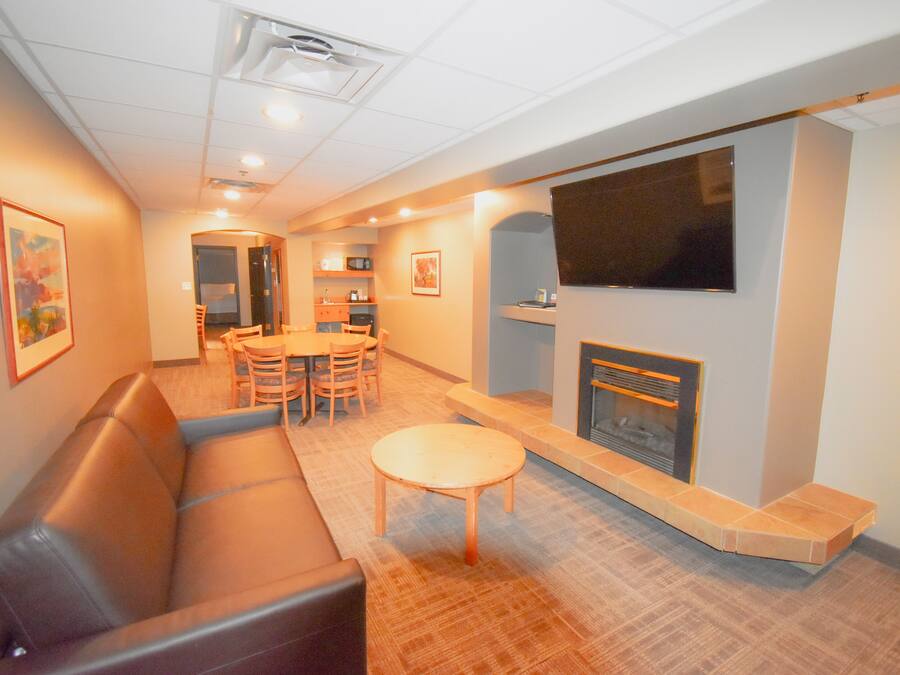 A living room with a brown leather sofa, a wooden coffee table, a fireplace, and a television mounted on the wall.